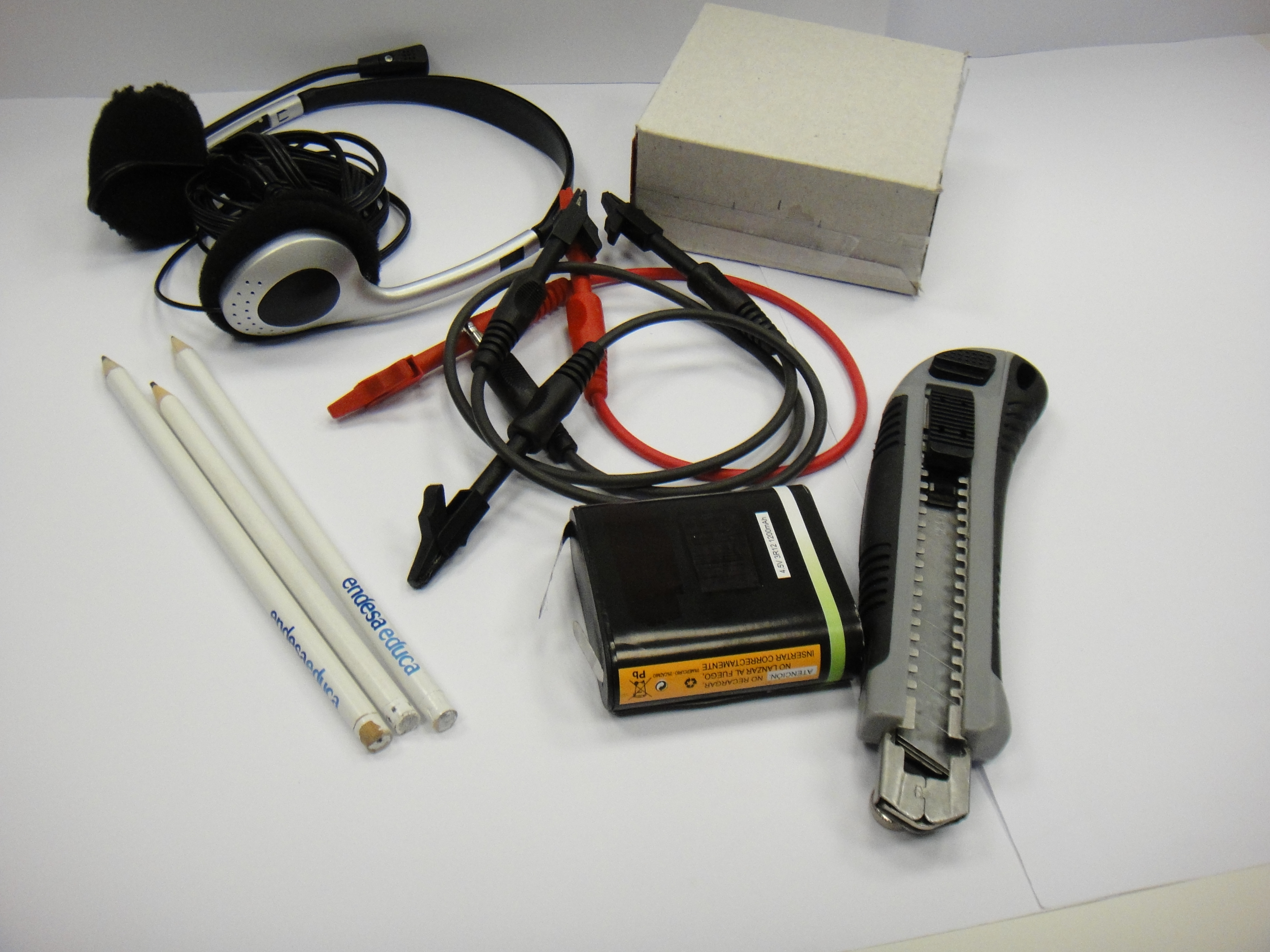 Materiales necesarios para construir un micrófono de carbón. Auriculares, lápices, una pila, 3 cables con cocodrilos y una caja de cartón.