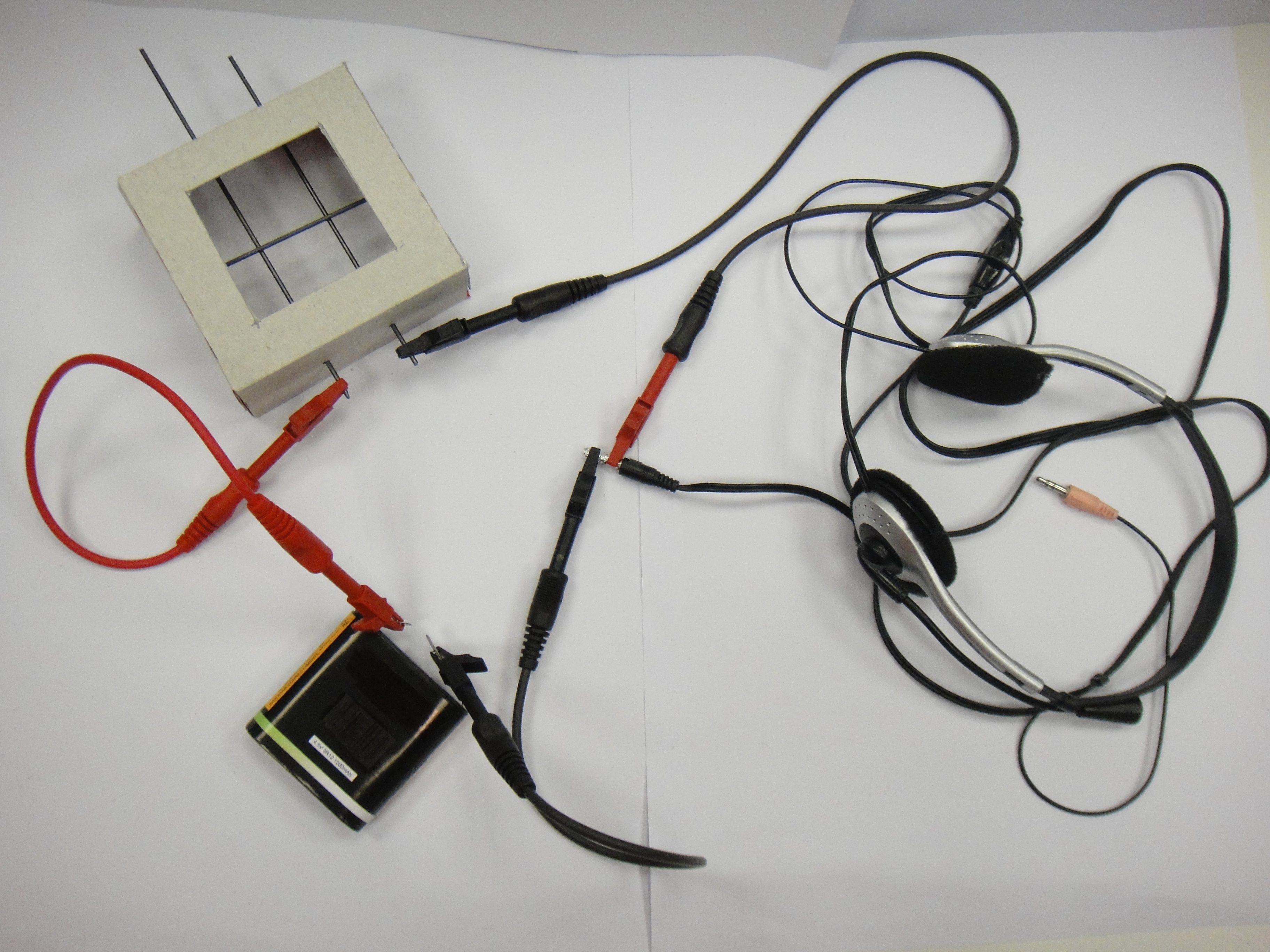 Materiales necesarios para construir un micrófono de carbón. Auriculares, lápices, una pila, 3 cables con cocodrilos y una caja de cartón.